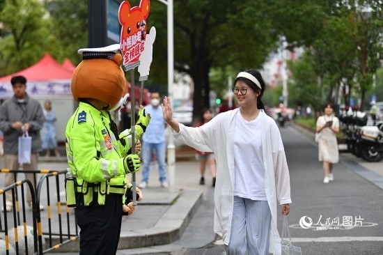 6月7日上午9時，隨著鈴聲的響起，2023年江西高考正式開考，江西省的53.57萬考生以縣（區(qū)）為單位隨機安排在全省256個考點、18968個考場參加高考。圖為“小熊交警”和考生擊掌鼓勵。 人民網(wǎng)記者 時雨攝