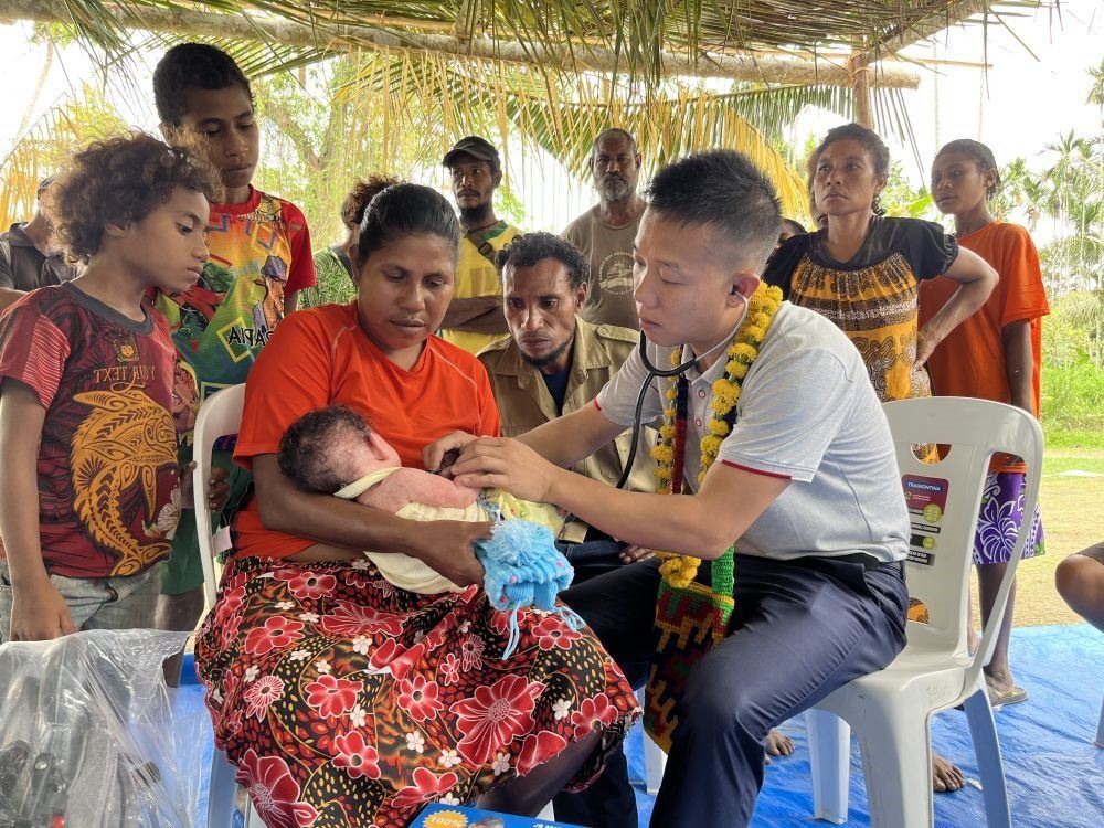 2023年8月5日，在巴布亞新幾內(nèi)亞中央省的一個(gè)村莊里，第12批援巴新中國(guó)醫(yī)療隊(duì)副隊(duì)長(zhǎng)、新生兒科副主任醫(yī)師劉振球?yàn)閶雰禾?lè)聽(tīng)診檢查。泰樂(lè)出生時(shí)患有重癥，一度生命垂危，經(jīng)過(guò)劉振球與當(dāng)?shù)蒯t(yī)護(hù)人員的救治最終痊愈。從2002年起，中國(guó)連續(xù)向巴新派出12批醫(yī)療隊(duì)，為提高巴新醫(yī)療衛(wèi)生水平作出積極貢獻(xiàn)。