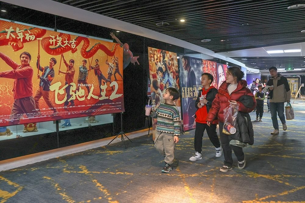 △ 2024年2月16日，在江西贛州一家電影院，觀眾從春節(jié)檔電影的宣傳展板前走過。