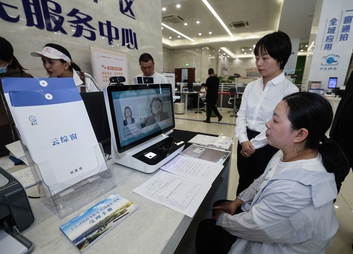 在浙江省嘉興市秀洲區(qū)王江涇鎮(zhèn)便民服務中心的“跨域通辦·云綜窗”窗口，辦理開業(yè)登記的個體工商戶（右一）通過該系統(tǒng)與江蘇省蘇州市吳江區(qū)盛澤鎮(zhèn)行政審批局工作人員視頻連線，進行身份讀取及材料線上審核（2024年5月9日攝）。新華社記者 徐昱 攝