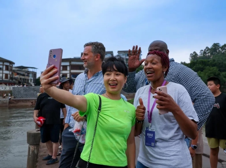 2024“一帶一路”媒體合作論壇聯(lián)合采訪調(diào)研行成員在樂山蘇稽古鎮(zhèn)與游客合影留念。本報記者 伊霄攝