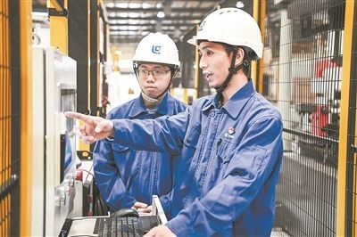 在廣西柳工機械股份有限公司生產(chǎn)車間內(nèi)，一名高級技師（右）給徒弟講解數(shù)控設(shè)備操作細節(jié)。新華社記者 曹祎銘攝