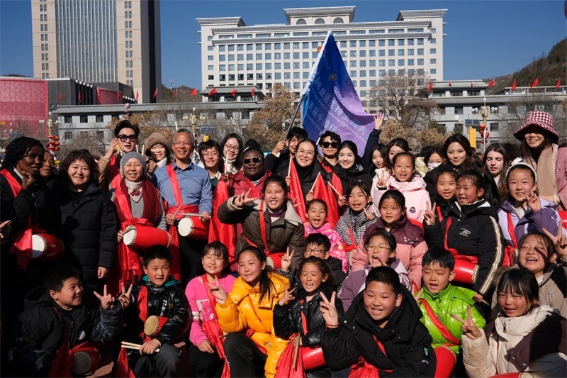 中外青年學子在安塞文化廣場觀看陜北腰鼓和大秧歌表演后合影留念，大家踏著鼓點共舞，翻飛的紅綢與躍動的身影交織，在黃土地廣場上繪出一幅生動的陜北民俗互動畫卷